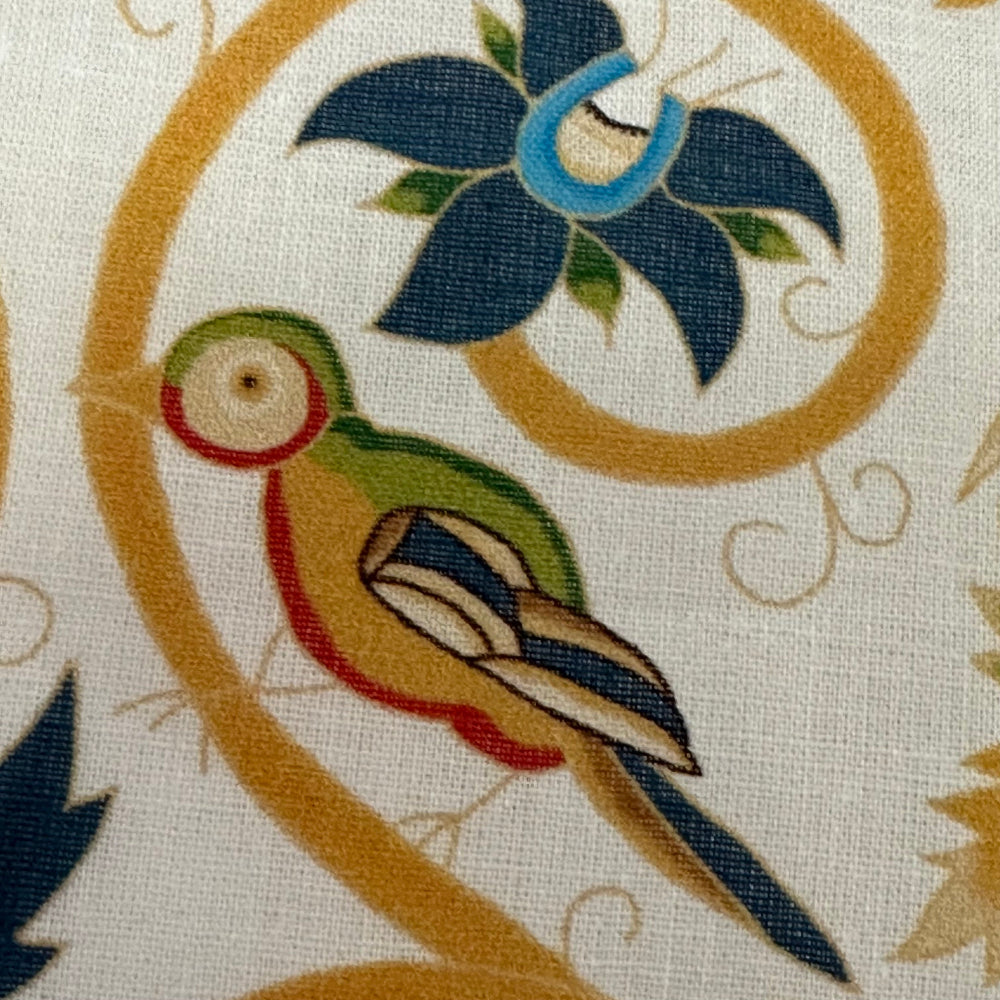 A fabric featuring an embroidered design with a bird, floral patterns, and detailed stitching in multiple colors on a light background.