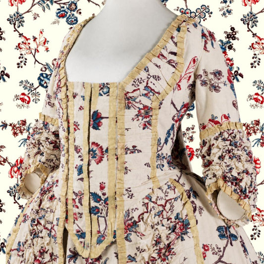 An antique-style 18th-century dress displayed on a white mannequin torso, featuring a beige base with a red and blue floral print and prominent gold ruffle trim.
